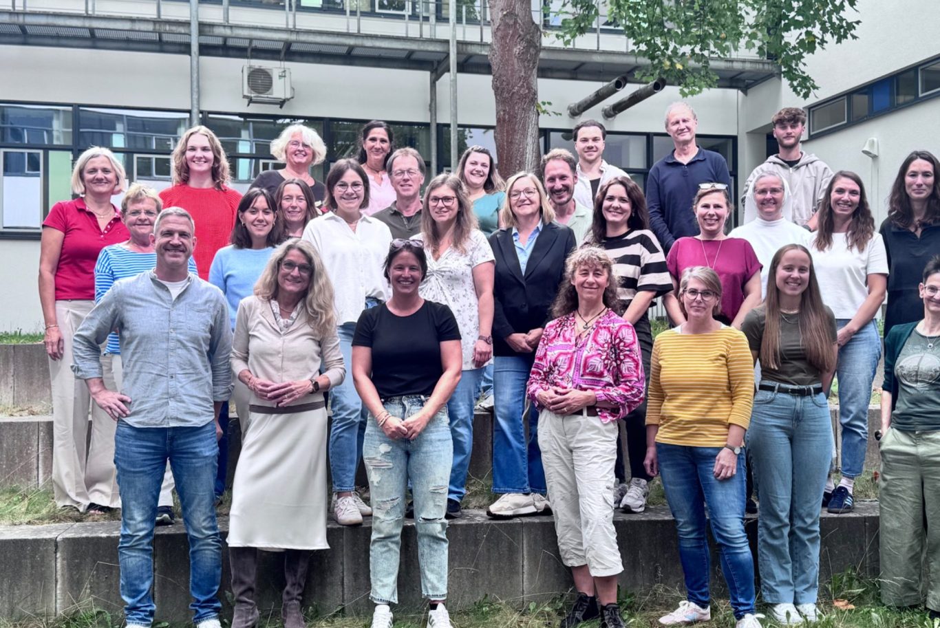 Gruppenfoto Kollegium GMS Gruppenfoto von 28 Personen im Freien, lächelnd und stehend auf einer Treppe.