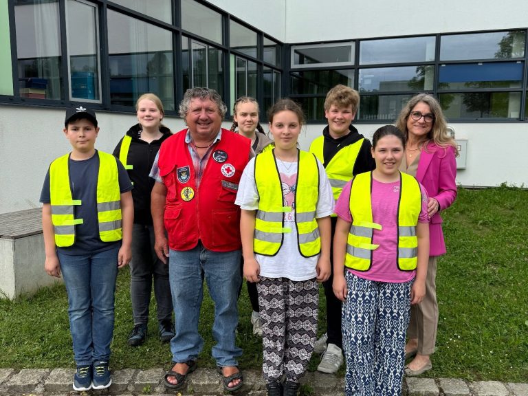 Schulsanitätsdienst Gruppenfoto von Kindern und Erwachsenen in gelben Warnwesten vor einem Gebäude.