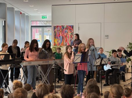 Eindrücke Bandklasse Schülergruppe führt ein Musikstück in einem Raum mit buntem Kunstwerk auf.