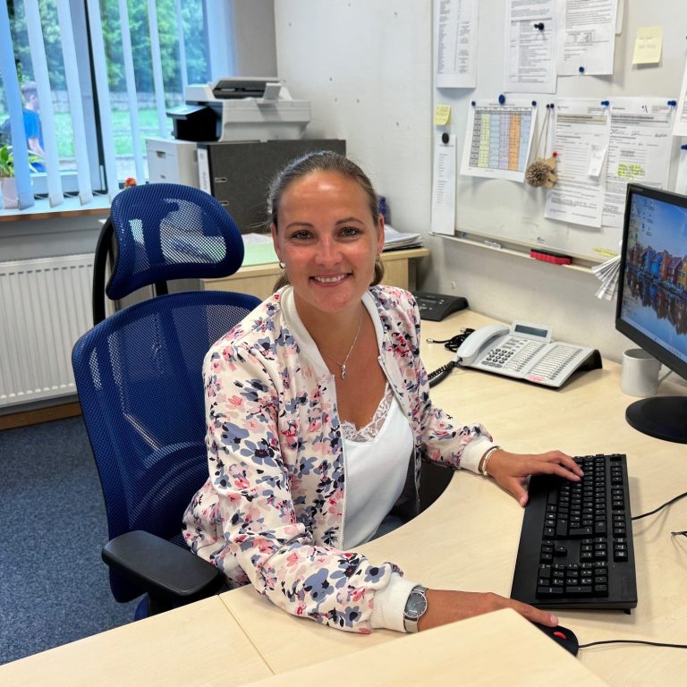 Sekretariat Frau lächelt am Schreibtisch vor einem Computer in einem Büroumfeld.