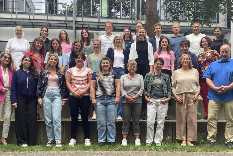Gruppenfoto Kollegium GMS Gruppenfoto von 28 Personen im Freien, lächelnd und stehend auf einer Treppe.