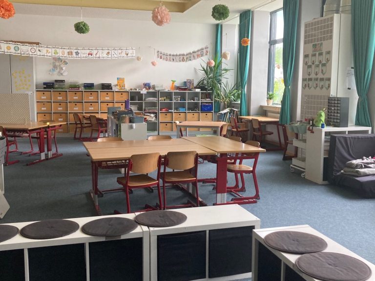 Churer Modell Heller Klassenraum mit Tischen, Stühlen und Regalen, dekoriert mit bunten Elementen.