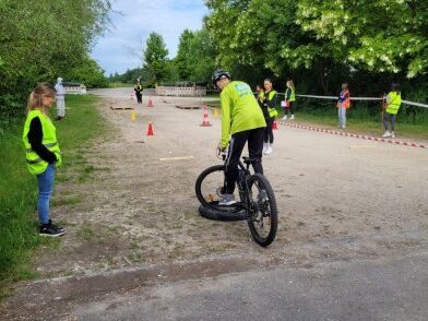 Mountainbike AG Person auf Fahrrad übt Fahrtechnik auf einem Übungsplatz, umgeben von Zuschauern.