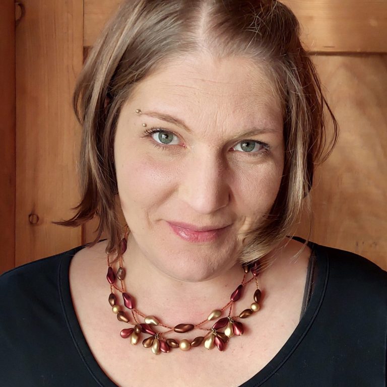 Petra Michallik Frau mit mittellangem Haar, trägt eine elegante Halskette und schaut freundlich.