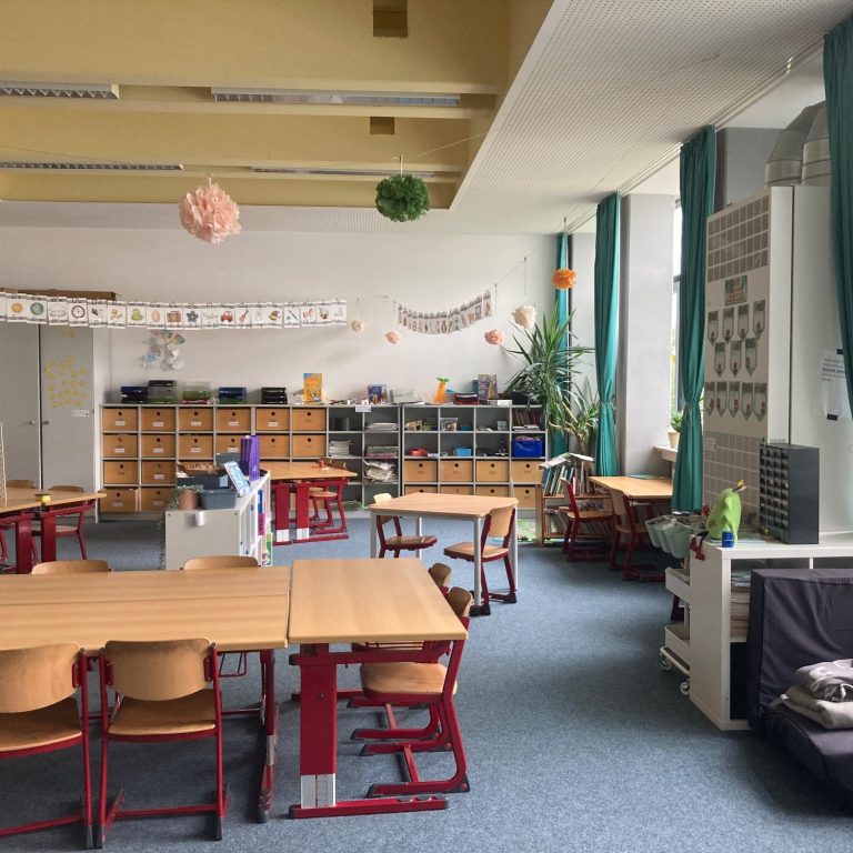 Churer Modell Leerer Klassenraum mit Tischen, Stühlen und Regalen, hellem Licht und Pflanzen.