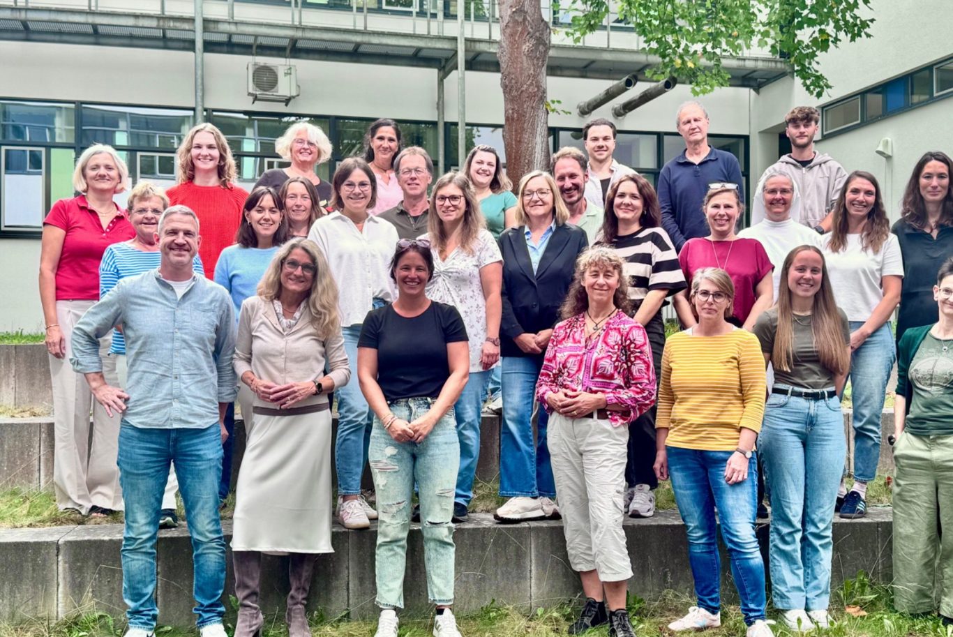 Gruppenfoto Kollegium GMS Gruppenfoto von 28 Personen im Freien, lächelnd und stehend auf einer Treppe.