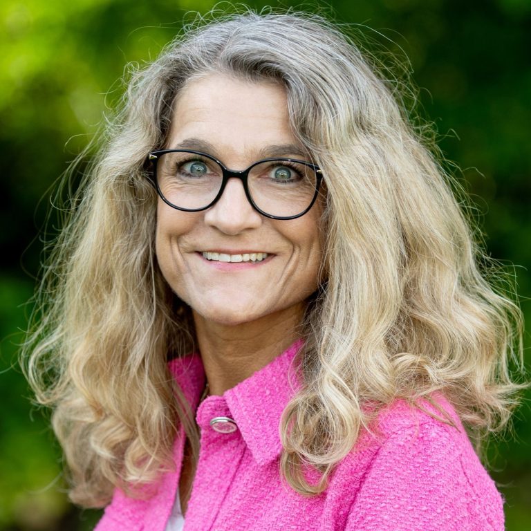 Simone Eisenbarth Konrektorin Frau mit langen, lockigen Haaren und Brille, lächelt vor grünem Hintergrund.