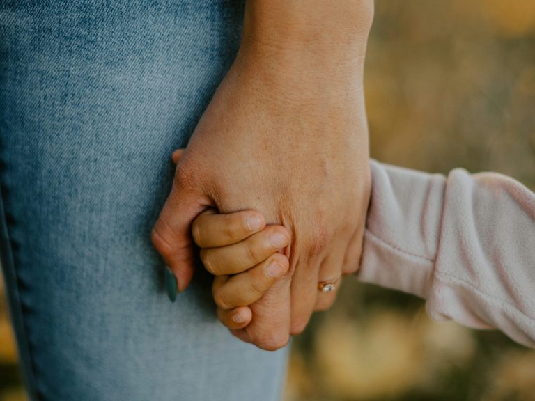 Jugendarbeit Händchen haltende Erwachsene und Kind im Freien, Hintergrund unscharf.