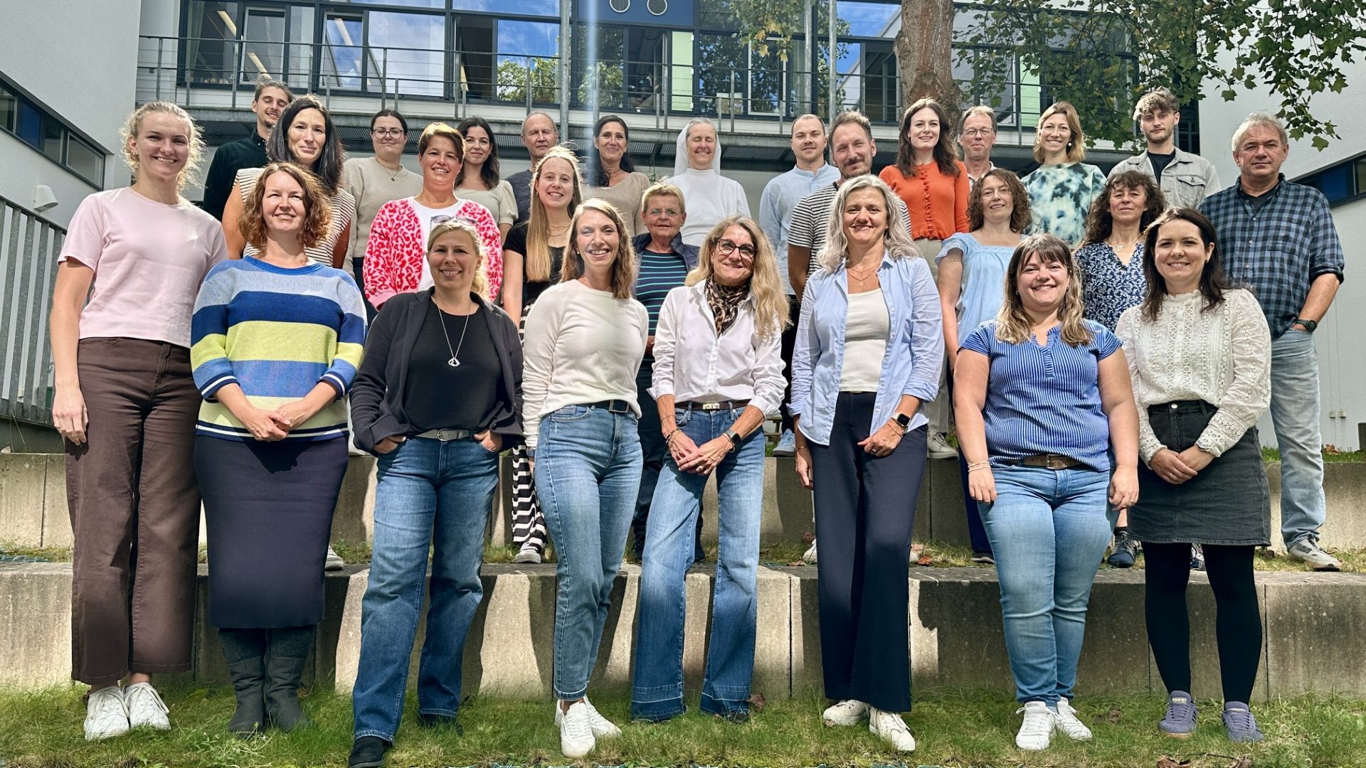 Kollegium der Grund- und Mittelschule Dinkelscherben Gruppenfoto von mehreren Personen in einem Garten, unterschiedliche Kleidung und Posen.