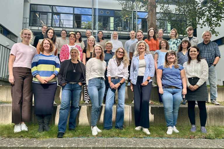 Gruppenfoto Kollegium GMS Gruppenfoto von 28 Personen im Freien, lächelnd und stehend auf einer Treppe.